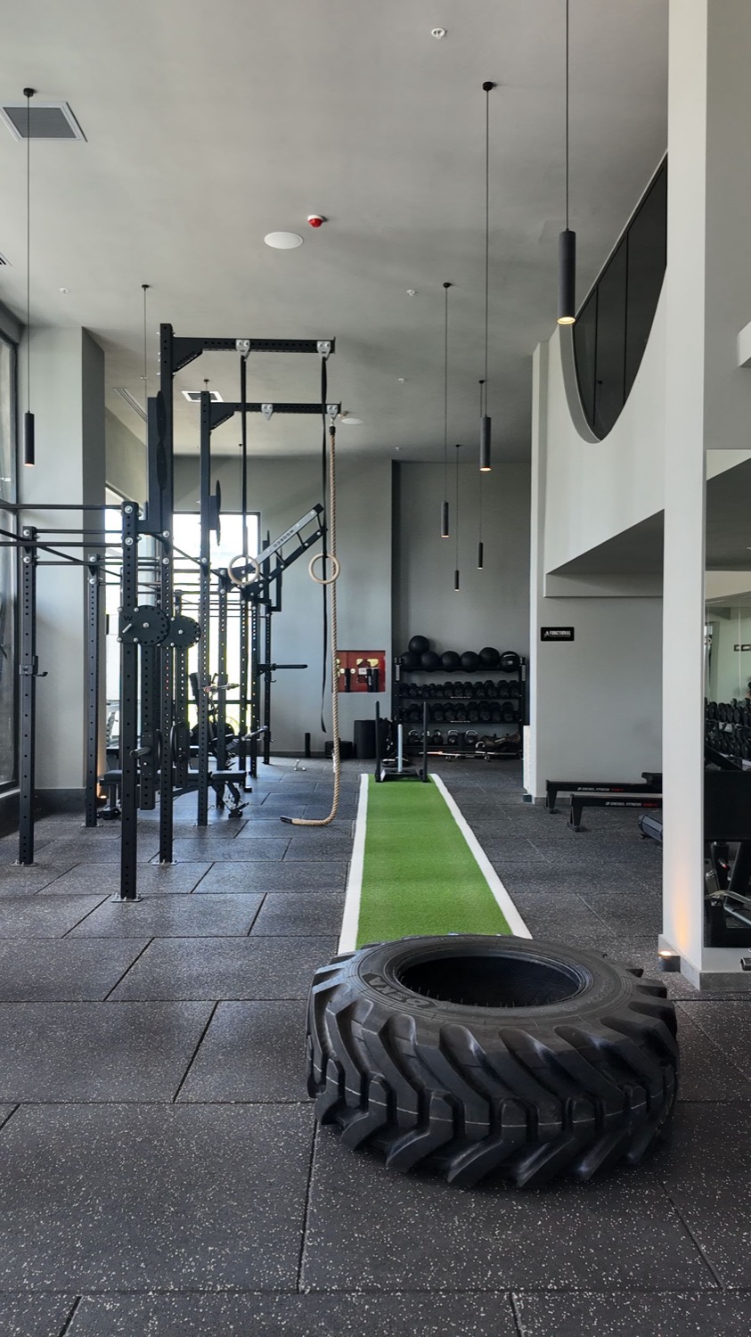 An empty gym floor with racks, turf lane and a training tire